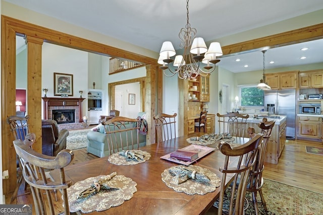 dining room featuring recessed lighting, a brick fireplace, a notable chandelier, and light wood finished floors