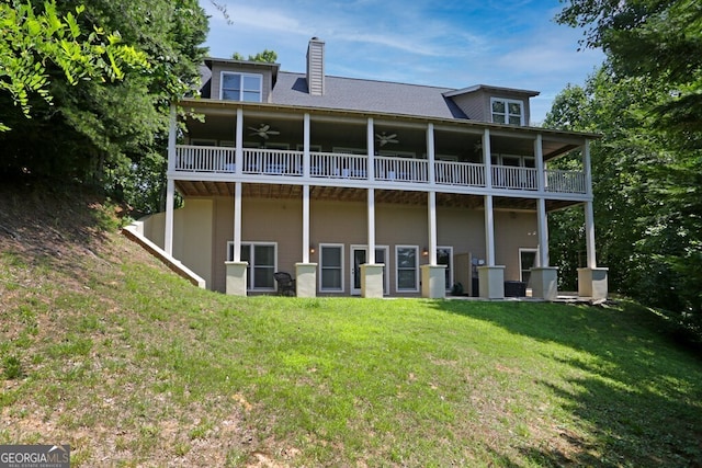 rear view of house with a yard, a chimney, a balcony, and a ceiling fan