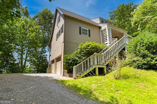 view of property exterior featuring gravel driveway, a garage, and stairs