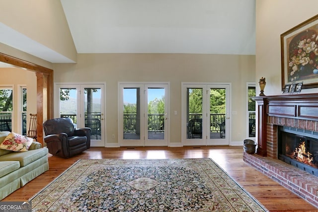 living room featuring high vaulted ceiling, a brick fireplace, baseboards, and wood finished floors