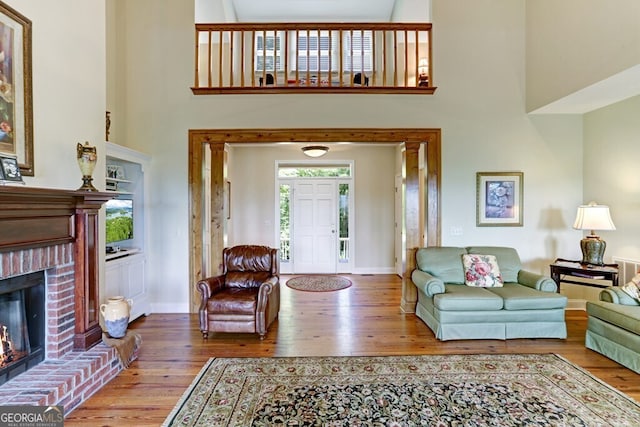 living room with a towering ceiling, a brick fireplace, baseboards, and wood finished floors