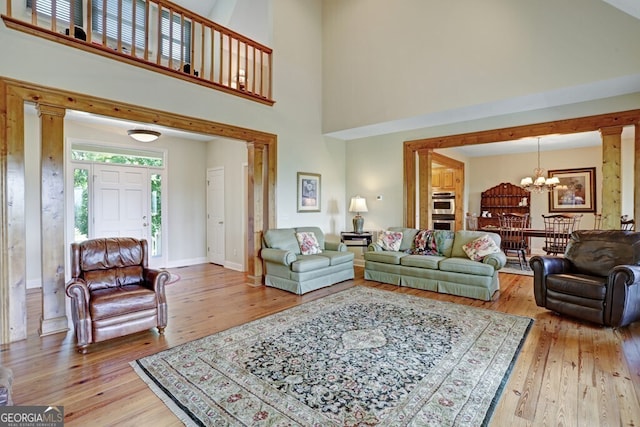 living area featuring a chandelier, a high ceiling, light wood-style flooring, and baseboards