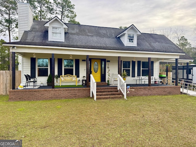 new england style home with a porch, a front yard, fence, and a chimney