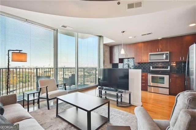 living room with light wood finished floors, floor to ceiling windows, and visible vents