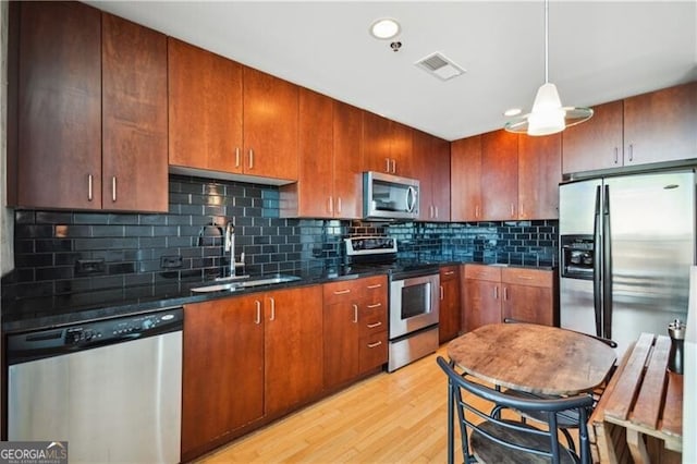 kitchen with stainless steel appliances, a sink, visible vents, backsplash, and light wood finished floors