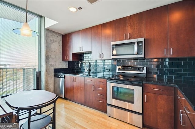 kitchen with tasteful backsplash, dark countertops, hanging light fixtures, light wood-style flooring, and appliances with stainless steel finishes