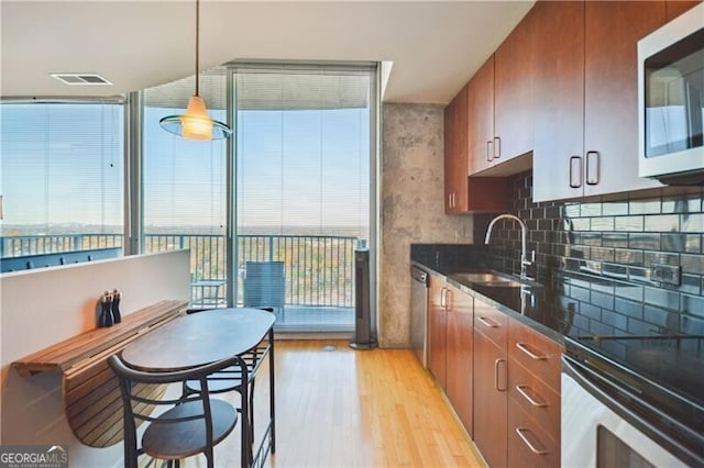 kitchen featuring visible vents, appliances with stainless steel finishes, light wood-style floors, brown cabinetry, and a sink