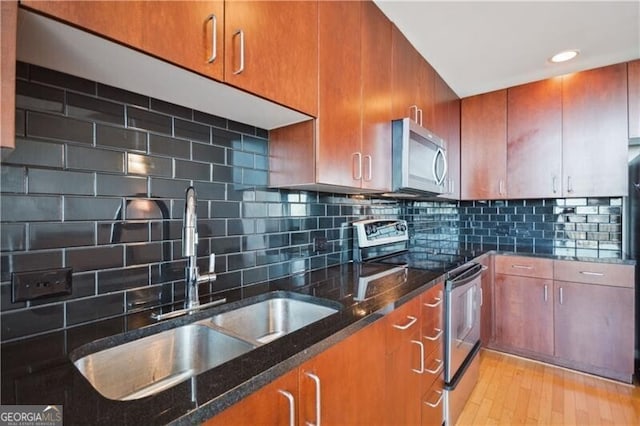 kitchen featuring brown cabinetry, decorative backsplash, dark stone counters, appliances with stainless steel finishes, and a sink