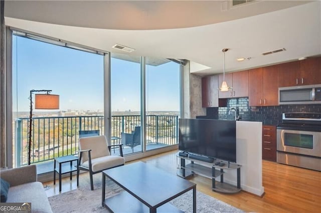 living room featuring expansive windows, light wood-style flooring, and visible vents