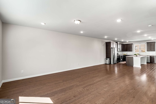 unfurnished living room featuring baseboards, dark wood-type flooring, and recessed lighting