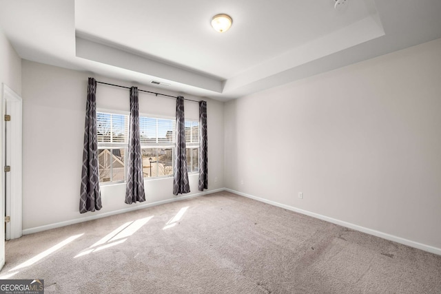 carpeted spare room with visible vents, baseboards, and a raised ceiling