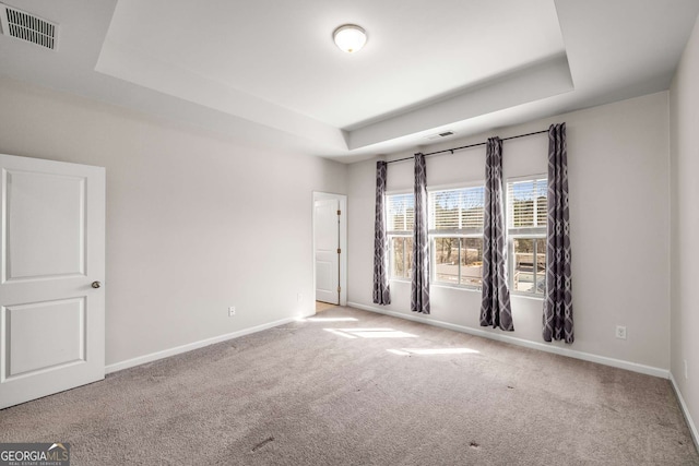 spare room with carpet, baseboards, visible vents, and a raised ceiling