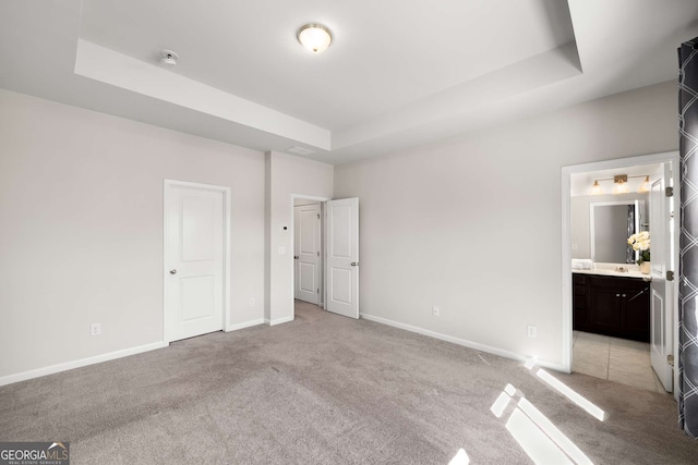 unfurnished bedroom featuring baseboards, a tray ceiling, and light colored carpet