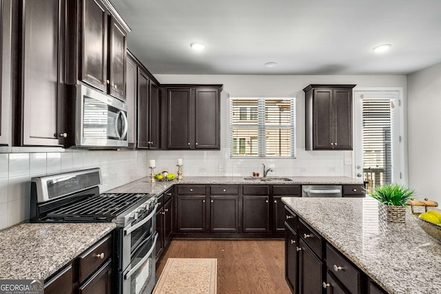 kitchen with stainless steel appliances, a sink, dark brown cabinets, decorative backsplash, and dark wood finished floors