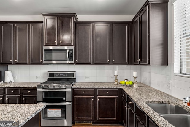 kitchen featuring appliances with stainless steel finishes, a sink, dark brown cabinetry, and tasteful backsplash