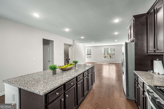 kitchen with light stone counters, dark wood-style flooring, a center island, stainless steel appliances, and dark brown cabinets