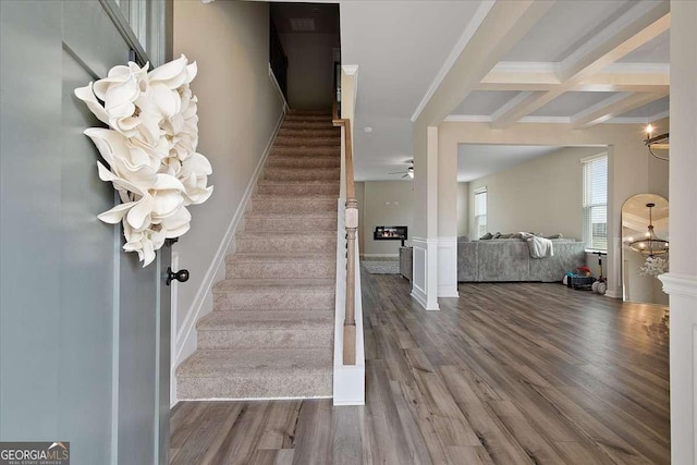 stairway with a lit fireplace, crown molding, beamed ceiling, and wood finished floors