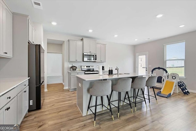 kitchen featuring light wood finished floors, visible vents, backsplash, appliances with stainless steel finishes, and a kitchen bar