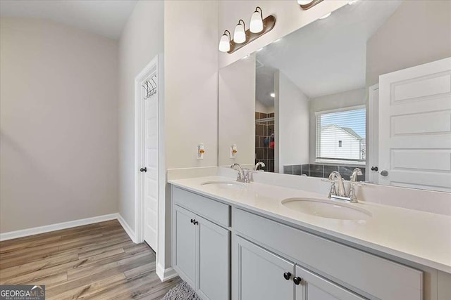 full bath featuring double vanity, a sink, baseboards, and wood finished floors