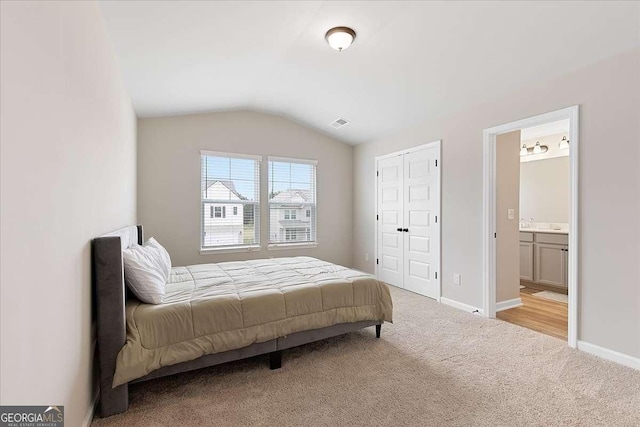 carpeted bedroom with ensuite bath, visible vents, baseboards, and vaulted ceiling