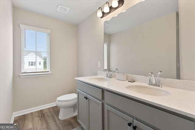 bathroom featuring double vanity, visible vents, toilet, a sink, and wood finished floors