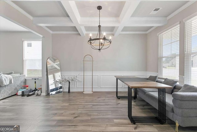 dining space with light wood-style floors, a wainscoted wall, beamed ceiling, and an inviting chandelier