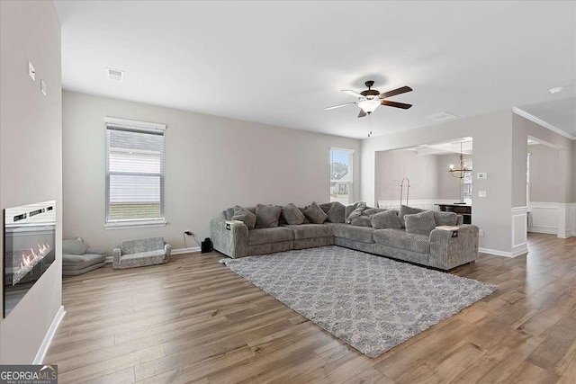 living area with ceiling fan with notable chandelier, visible vents, wood finished floors, and a glass covered fireplace