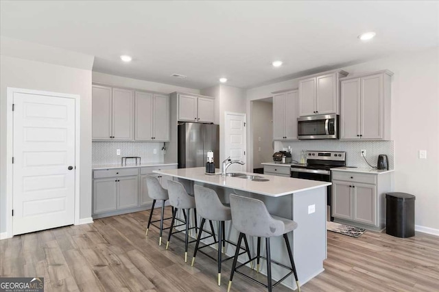 kitchen featuring appliances with stainless steel finishes, gray cabinets, a kitchen bar, and a sink