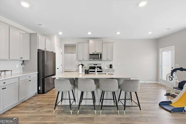 kitchen with visible vents, appliances with stainless steel finishes, light wood-style flooring, and a breakfast bar area