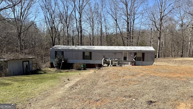 manufactured / mobile home featuring a forest view, a front yard, and an outdoor structure