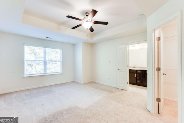 unfurnished bedroom featuring light carpet, visible vents, baseboards, a ceiling fan, and a tray ceiling