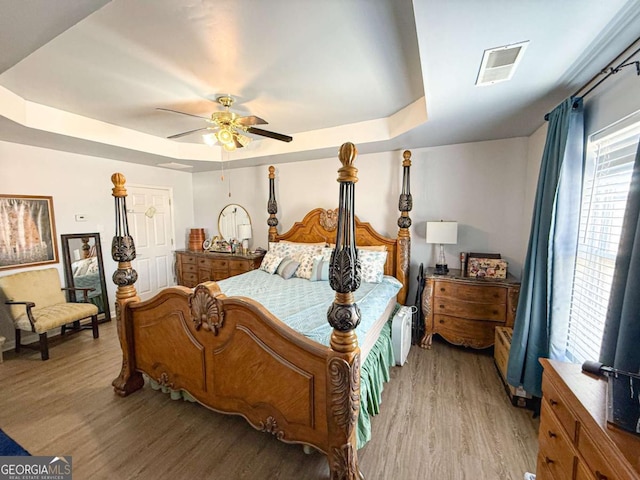 bedroom with a raised ceiling, visible vents, ceiling fan, and light wood-style flooring