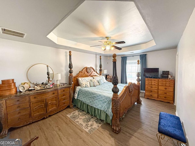 bedroom featuring light wood finished floors, ceiling fan, a tray ceiling, and visible vents