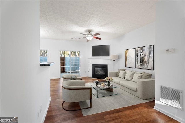 living area featuring visible vents, a textured ceiling, a glass covered fireplace, and wood finished floors