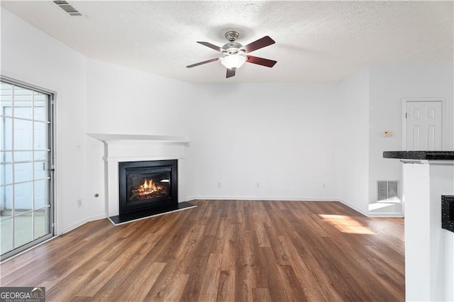 unfurnished living room with a glass covered fireplace, a textured ceiling, visible vents, and wood finished floors