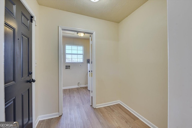 hallway with light wood finished floors, baseboards, and a textured ceiling