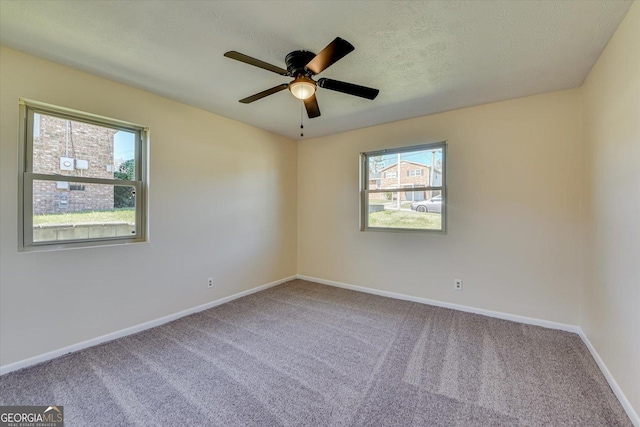 carpeted empty room with a healthy amount of sunlight, a ceiling fan, baseboards, and a textured ceiling