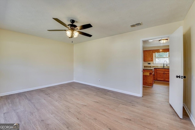 empty room featuring a textured ceiling, light wood finished floors, visible vents, and baseboards