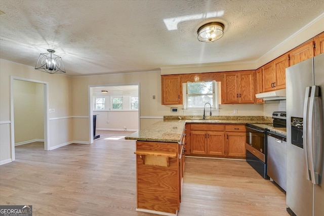 kitchen with under cabinet range hood, a peninsula, a sink, appliances with stainless steel finishes, and brown cabinets