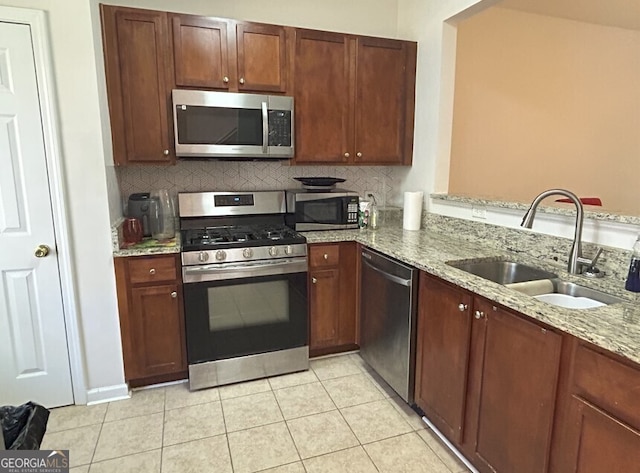 kitchen featuring light stone counters, light tile patterned floors, stainless steel appliances, decorative backsplash, and a sink