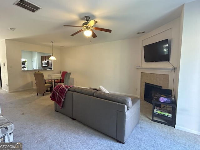 carpeted living area featuring ceiling fan, a fireplace, visible vents, and baseboards