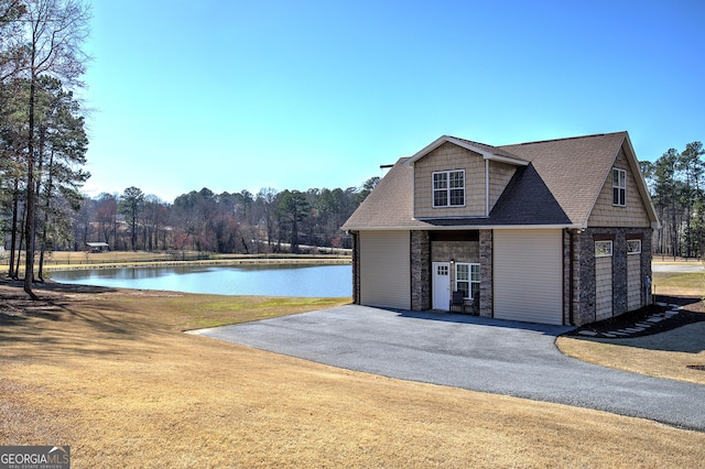 view of front of house with a shingled roof, a water view, a front yard, stone siding, and driveway