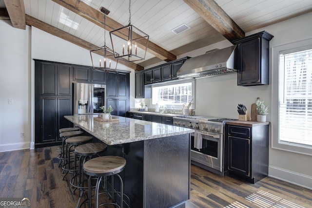 kitchen with a wealth of natural light, appliances with stainless steel finishes, a kitchen island, and wall chimney range hood