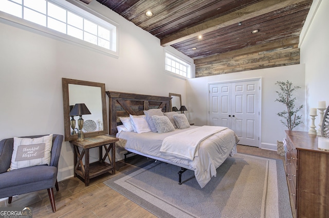 bedroom featuring wood finished floors, baseboards, beam ceiling, a closet, and wooden ceiling