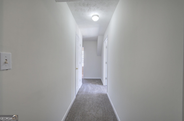 corridor featuring baseboards, carpet floors, and a textured ceiling