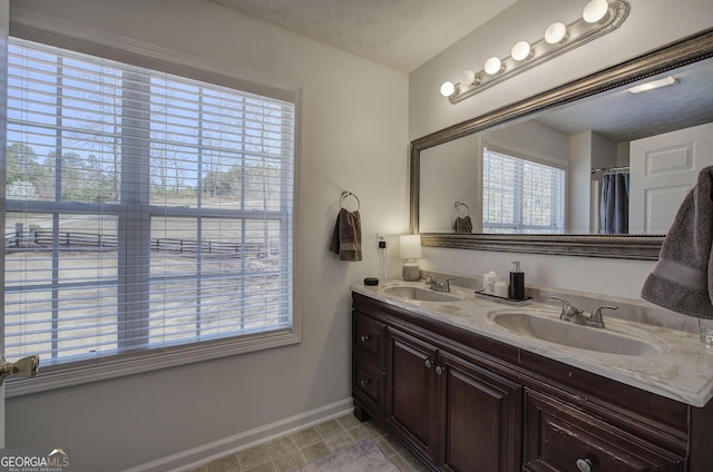 bathroom featuring a textured ceiling, double vanity, baseboards, and a sink