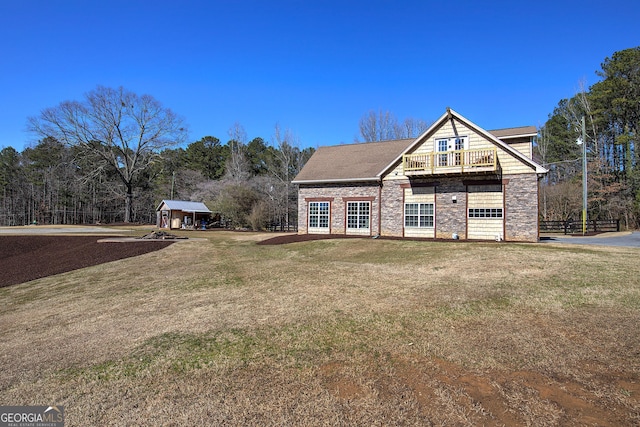 view of front of property featuring stone siding, a balcony, and a front lawn