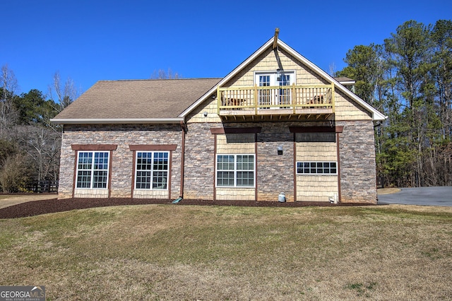 back of house with a balcony, roof with shingles, and a lawn