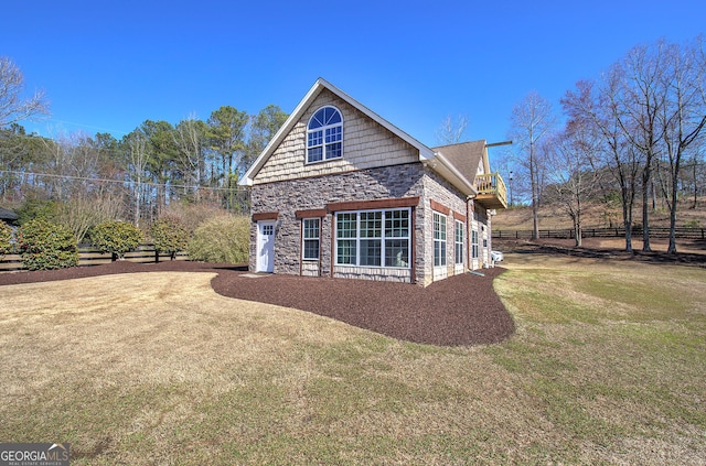 view of side of home with stone siding, driveway, a yard, and fence