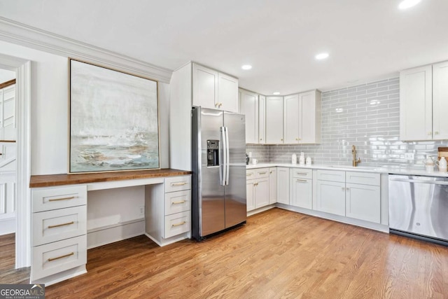 kitchen with light wood finished floors, stainless steel appliances, backsplash, and built in study area